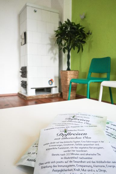 Ein Raum mit grüner Wand, einem alten Kamin, einem Stuhl und Informationsblättern.