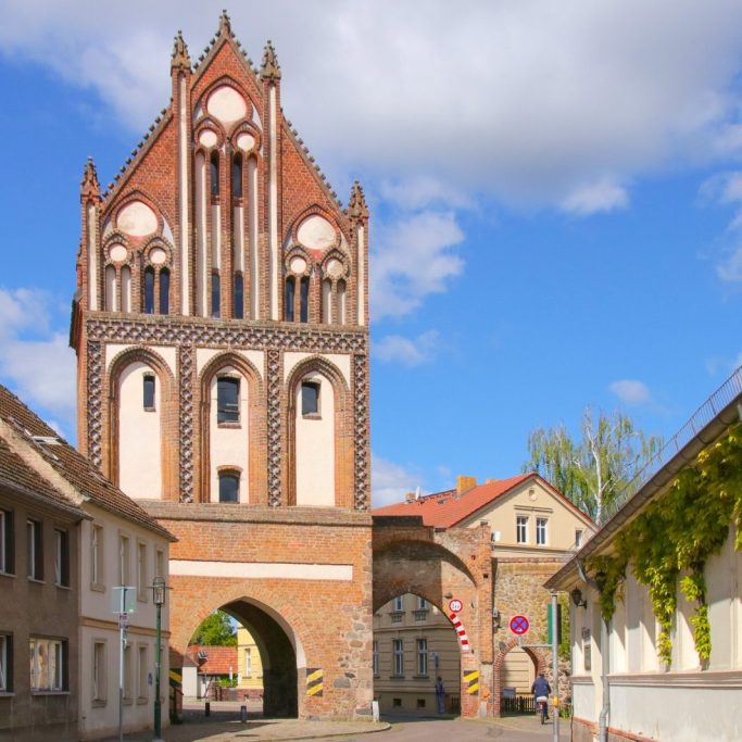 Historisches Stadttor von Gransee mit rot-weißer Fassade und blauen Himmel im Hintergrund.