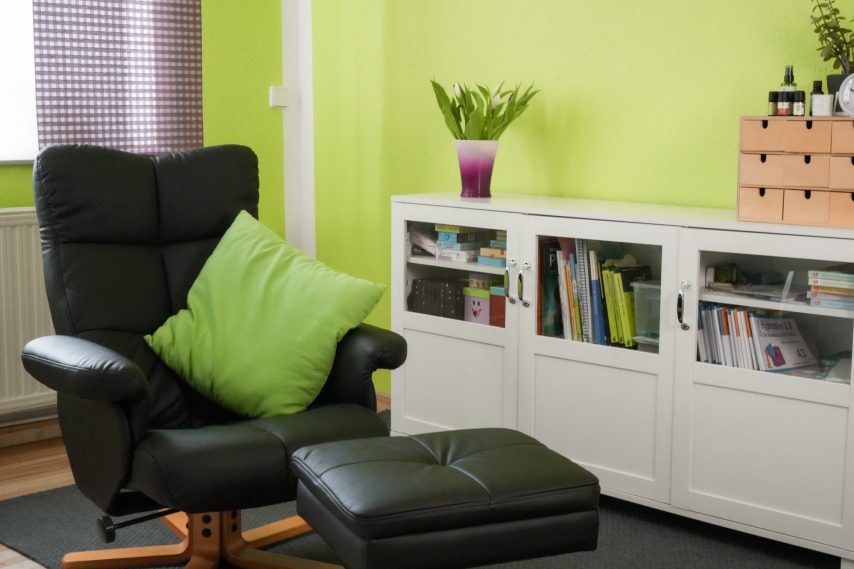 Schwarzer Relaxsessel mit grüner Kissen, weinfarbener Vase und white sideboard im Raum.