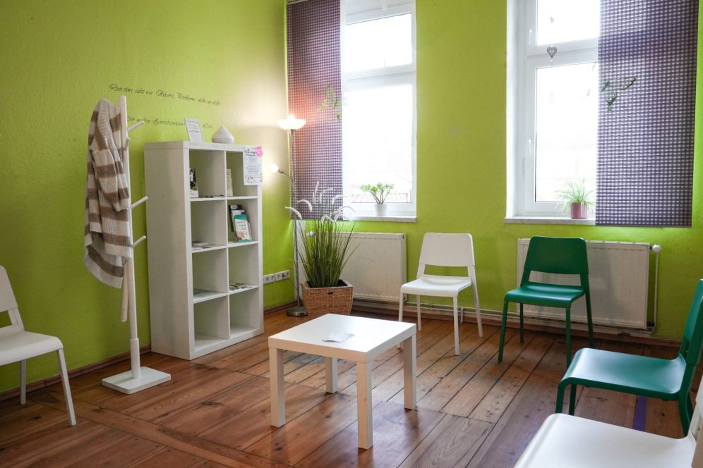Helle, grüne Wartebereich mit weißen und grünen Stühlen sowie einem kleinen Tisch.
