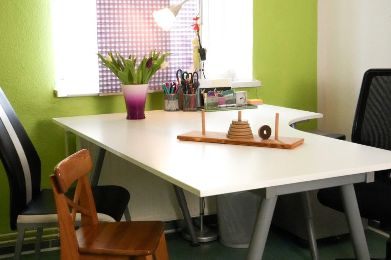 Ein moderner Schreibtisch mit Pflanzen, Stiften und Stühlen in einem grünen Raum.